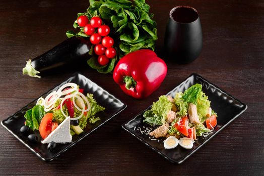 Greek salad, Caesar on black square plates on dark wooden table