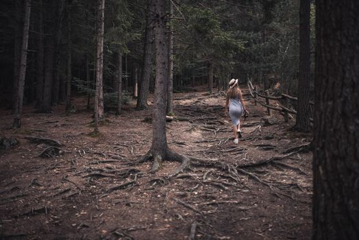 Slavic tanned fair-haired young girl with a boater hat on nature. Traveler tourist in a dark forest. constant tone of clothes. dark brown background