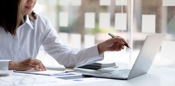 Close up Businesswoman hand holding pen and pointing at financial paperwork, financial charts to analyze profit concept.