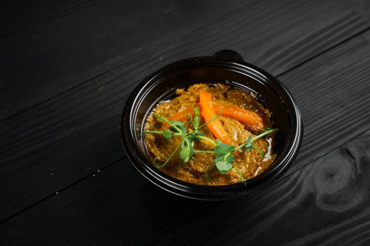 Hummus garnished with peppers and herbs in black plate on dark wooden table