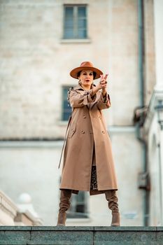 Outdoor fashion portrait of young elegant fashionable brunette woman, model in stylish hat, choker and light raincoat posing at sunset in European city