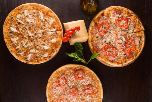 Pizza with chicken, mushrooms, cheese, sauce, ham, salami and pepper, tomatoes on a dark wooden table. Assortment of pizzas.