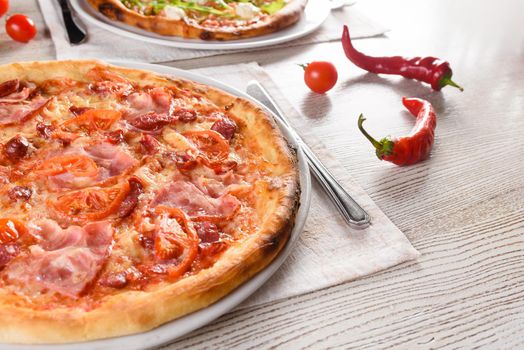 Pizza with chicken, mushrooms, cheese, sauce, ham and salami, pepper chili, tomatoes on a dark wooden table