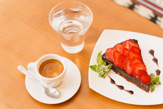 Chocolate cake, brownie with strawberries and mint, espresso, glass of water on a wooden table.