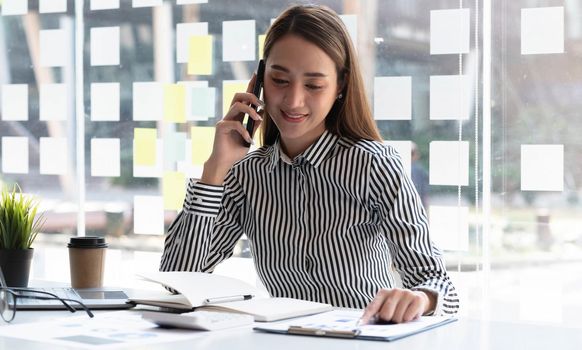 Charming Asian woman with a smile standing point papers and use mobile phone at the office..