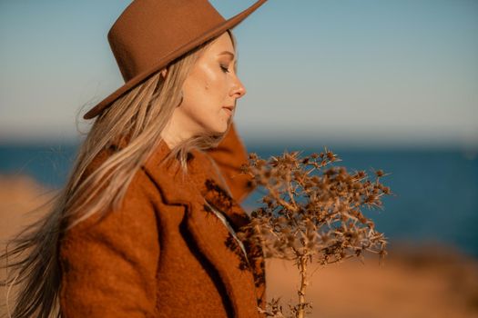 A woman walking along the coast near the sea. An elegant lady in a brown coat and a hat with fashionable makeup walks on the seashore.