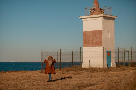 A woman walking along the coast near the sea. An elegant lady in a brown coat and a hat with fashionable makeup walks on the seashore.