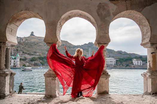 View of Balaklava Bay through an arched balcony in oriental style. The girl in a long red dress stands with her back. Abandoned mansion on the Black Sea coast.