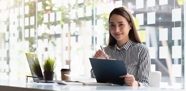 Young Asian businesswoman taking notes using a tablet at the modern office.Looking at the camera..