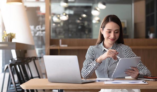 Happy young asian businesswoman sitting on her workplace in the office. Young woman working at laptop in the office..