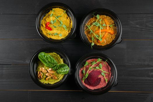 Hummus garnished peppers, chili, beet and herbs in black bowl on dark wooden table. Hummus assortment.