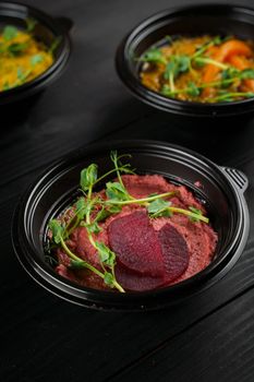 Hummus garnished peppers, chili, beet and herbs in black bowl on dark wooden table. Hummus assortment.