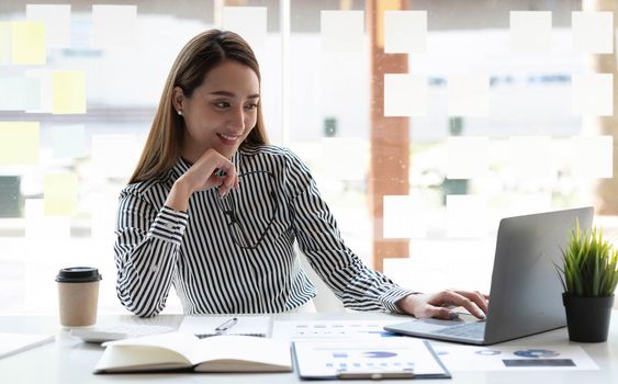 Beautiful young asian woman sitting at coffee shop using laptop. Happy young businesswoman sitting at table in cafe with tab top computer..