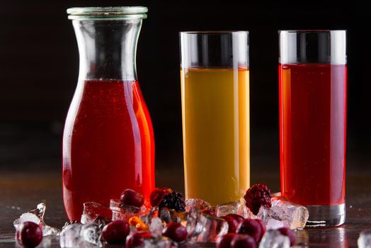 Compote berry, fruit in a jar and glasses on a dark wooden table. Summer lemonade. Decorated with ice and cherries, raspberries