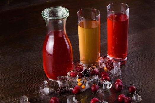 Compote berry, fruit in a jar and glasses on a dark wooden table. Summer lemonade. Decorated with ice and cherries, raspberries