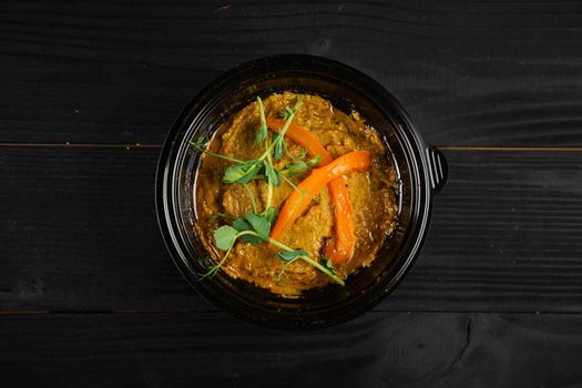 Hummus garnished with peppers and herbs in black plate on dark wooden table