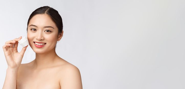 Beautiful young woman on white isolated background holding cosmetic face cream, asian.