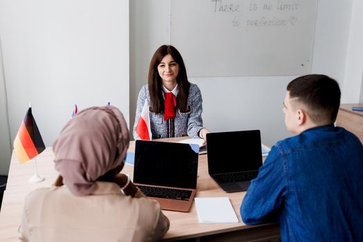 Multiethnic students and teacher study foreign languages together in class. Studing with laptop. Black handsome girl student study with white people together and look into camera