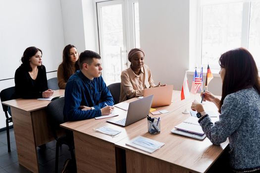 Multiethnic students and teacher study foreign languages together in class. Studing with laptop. Black handsome girl student study with white people together and look into camera