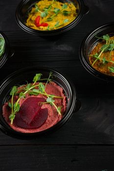 Hummus garnished peppers, chili, beet and herbs in black bowl on dark wooden table. Hummus assortment.