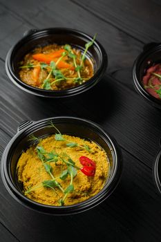 Hummus garnished peppers, chili, beet and herbs in black bowl on dark wooden table. Hummus assortment.