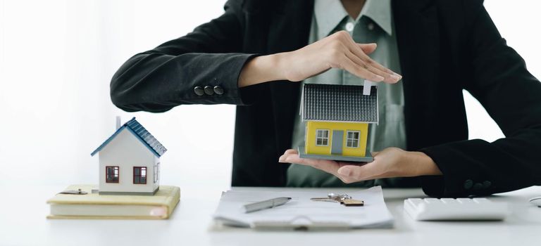 Miniature house in the hands of an Asian woman real estate agent home loan working at the office.
