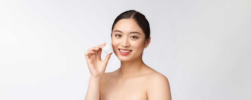 Beautiful young woman on white isolated background holding cosmetic face cream, asian.