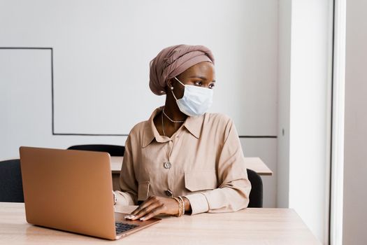 African black woman with laptop. Using computer for on-line work. Medical mask for protection against coronovirus covid-19.