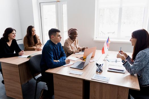 Multiethnic students and teacher study foreign languages together in class. Studing with laptop. Black handsome girl student study with white people together and look into camera