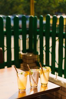 Cocktails with lemon and mint in glasses with tube on a wooden table against the background of a restaurant. Cold lemonade