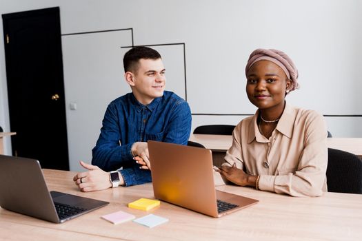 Muslim black girl and white man with laptop. Multiethnic couple work online together on business project. Working at home. Surfing internet.