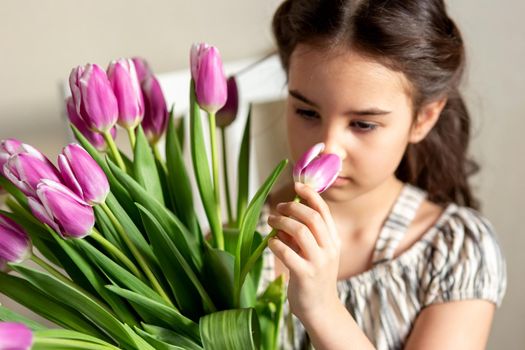 Portrait of a beautiful little girl with a bouquet of tulips, sniffs the aroma of a bud. Close up