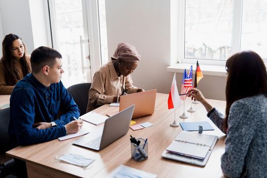 Multiethnic students and teacher study foreign languages together in class. Studing with laptop. Black handsome girl student study with white people together and look into camera