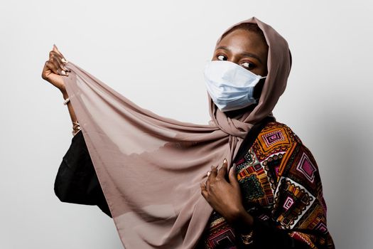 Black muslim in medical mask weared in hijab on white backgroud. Successful black girl. Attractive african girl in national dress in studio