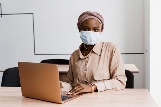 African black woman with laptop. Using computer for on-line work. Medical mask for protection against coronovirus covid-19.