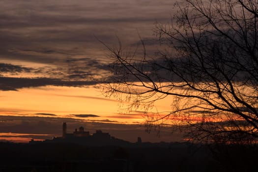 A tree silhouette in the foreground and La Seu Vella Cathedral in the background with an orange cloudy sky in sunset