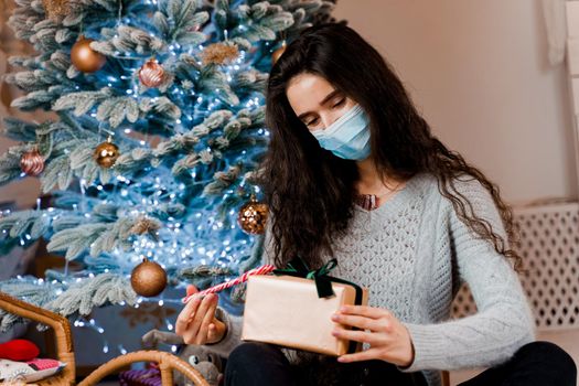 Girl in a medical mask with a Christmas present and candy. celebration of the new year on self-isolation. Pandemic coronavirus covid-19 concept. Advertising sale during the quarantine period