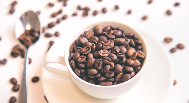 white cup and coffee beans on a white background. Selective focus.