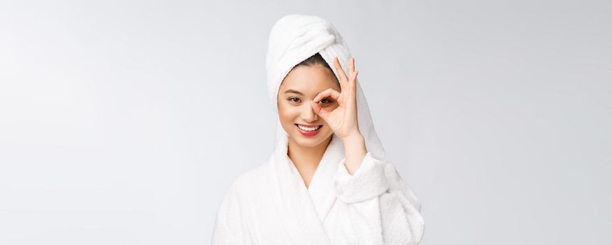 Close up of young smiling woman with finger ok gesture on eyes, isolated on white background.