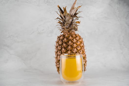 Pineapple fruit and juice in double glass cup on white stone background. Tropical fruit Pouring yellow tropical juice into glass.