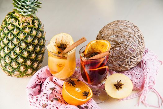 Mulled wine, grog and punch hot alcohol drinks on the table with seasonal decoration: pineapple, cinnamon, apple, orange, star anise. Seasonal spiced drink.