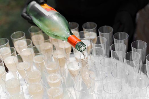 Waiter pours champagne into wine glass. Welcome drink zone. Waiter in black gloves holds sparkling wine bottle.