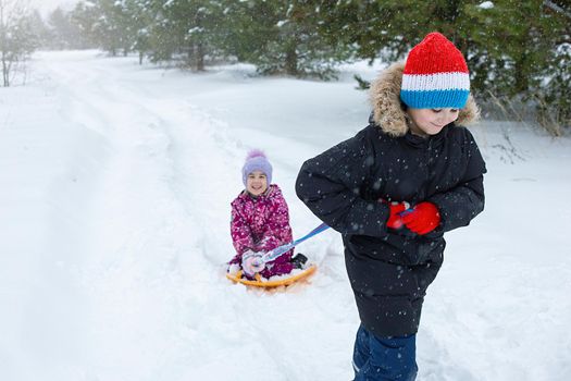 Winter games outside. A teenage boy rolls a little girl in the snow on a plastic ice rink. copy space