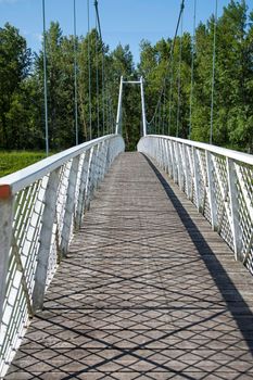 View of a white suspended bridge with wooden tread and blue sky with clouds