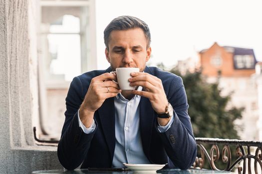 Man like coffee. Handsome man with cup of coffee in cafe. Morning lifestyle of male. Man is sitting on the summer terrace in cafe, drinking coffee and smiling