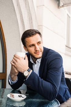 Man like coffee. Handsome man with cup of coffee in cafe. Morning lifestyle of male. Man is sitting on the summer terrace in cafe, drinking coffee and smiling