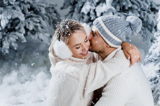 Winter love story at the eve of new year celebration. Couple hugging near christmass trees. Winter holidays. Love story of young couple weared white pullovers. Happy man and woman love each other.