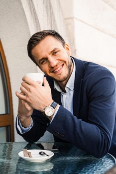 Man like coffee. Handsome man with cup of coffee in cafe. Morning lifestyle of male. Man is sitting on the summer terrace in cafe, drinking coffee and smiling