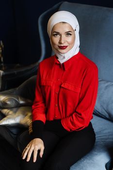 Attractive muslim caucasian girl weared head scarf is sitting on the sofa. Islam religion