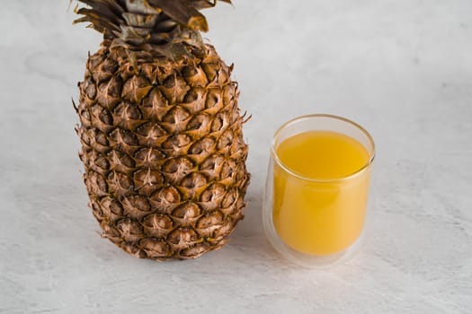 Pineapple fruit and juice in double glass cup on white stone background. Tropical fruit Pouring yellow tropical juice into glass.